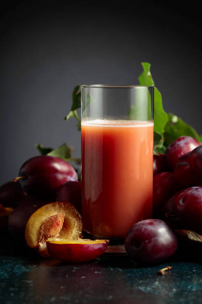Glass of plum juice on a table with fresh purple plums. Copy space.