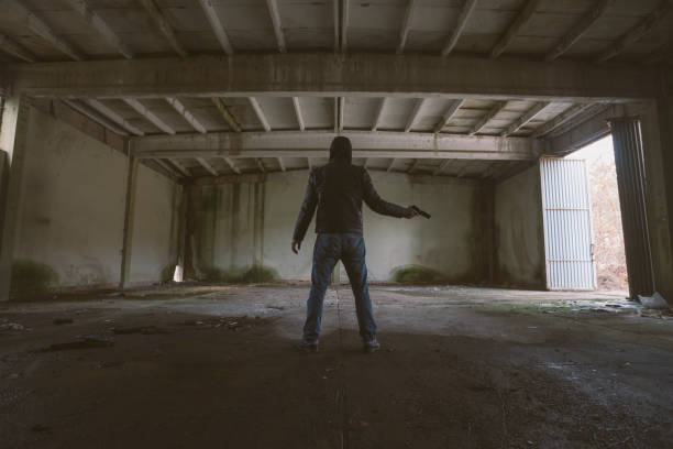 istock Man with gun at large abandoned dark building 1356022083