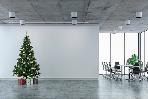 Empty office interior on concrete floor with a green and golden Christmas tree in front of an empty white wall background and copy space, conference table, potted plant and windows in background. 3D rendered image.