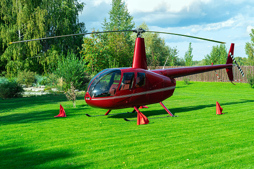 The red helicopter landed on a green lawn, the landing place is marked with red flags