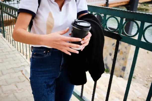Woman spill coffee from paper cup to white shirt and jeans. Large coffee spot on white shirt