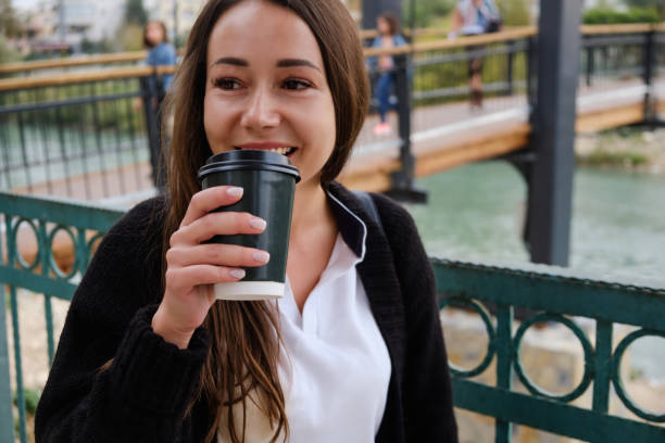istock Smiling young woman drinks coffee outside 1356026204