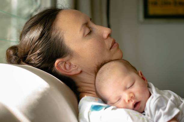 Tired exhausted mother taking a nap with her baby at home. Motherhood and maternity. stock photo