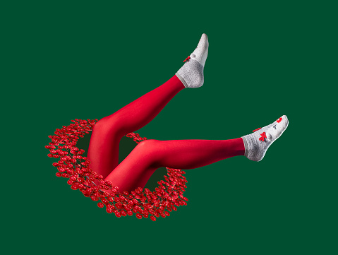 istock Collage surrealista navideño con piernas de mujer en medias rojas y calcetines cálidos de invierno con orejas de reno caídas en un agujero mágico con corona de Navidad 1356028654