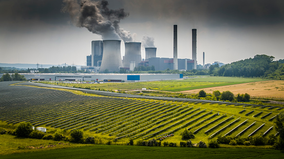 Aerial view of a solar power station in front of a coal fired power station. Sustainable renewable electricity VS fossil fuels (lignite)\nShot in Germany, Europe.