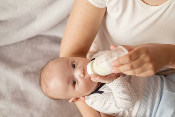 istock baby eats milk from a bottle and looks at camera 1356038667