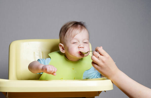 istock little child eats on gray background, mom feeds the baby with a spoon 1356040616