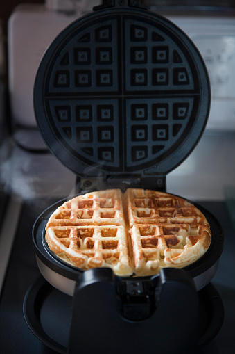 Steamy crunchy golden homemade waffle cooking in waffle maker