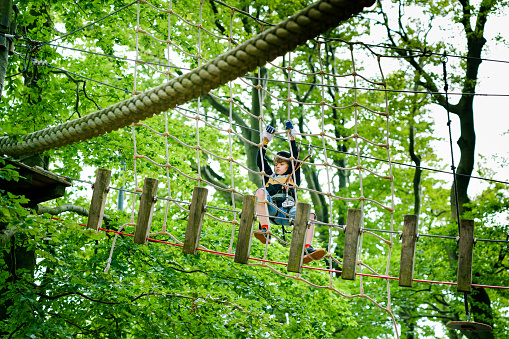 School boy in forest adventure park. Acitve child, kid in helmet climbs on high rope trail. Agility skills and climbing outdoor amusement center for children. Outdoors activity for kid and families