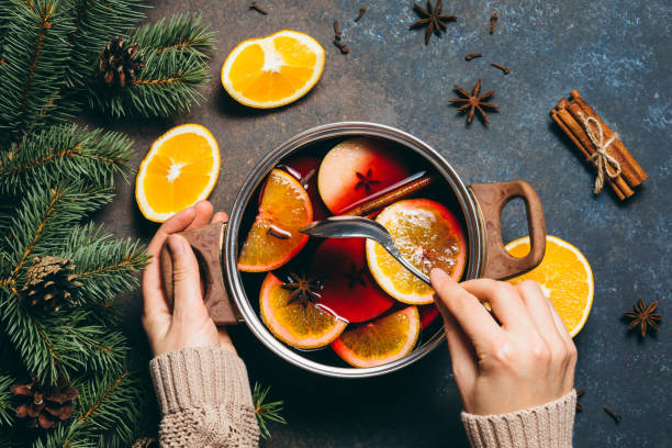 Hot Mulled wine cooking at home for happy christmas time. Red wine, orange, apple and spices - ingredients boiling in a pot on dark background. Warming new year and holiday drink, flat lay. stock photo