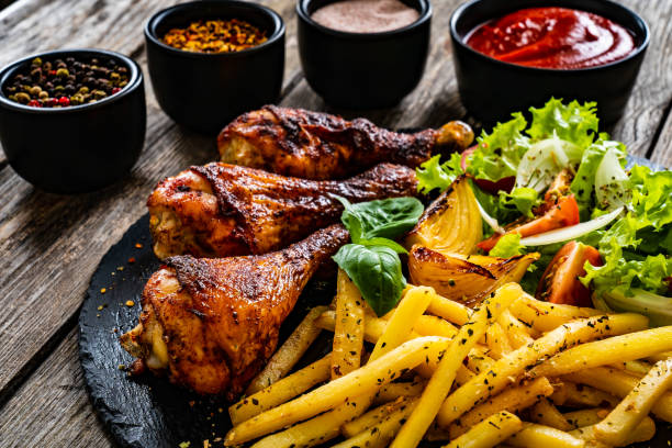 Barbecue chicken drumsticks with chips and greens on wooden table stock photo
