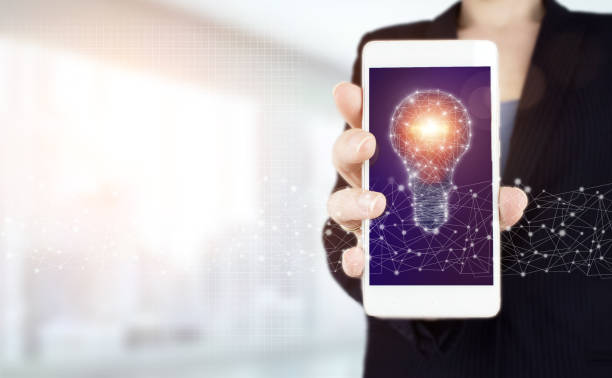istock Innovation, brainstorming, inspiration and solution concepts. Hand hold white smartphone with digital hologram light bulb sign on light blurred background. Innovation and creative idea concept. 1356053590