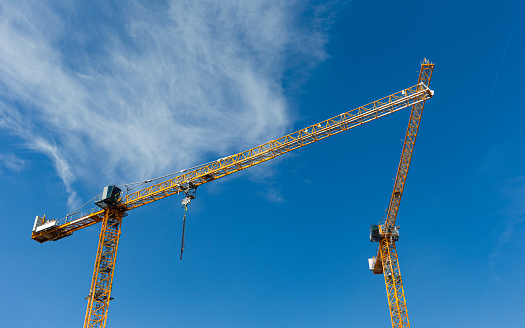 Daytime view of two tower cranes against a blue sky, looking to be one, a unity