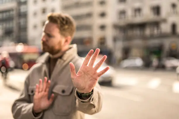 Young man standing on city street and making refusal gestures. Focus on foreground.