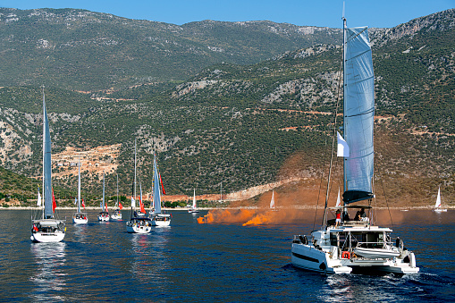 Orange colored smoke grenade in the blue sea with sailboats in Kas (Kaş) district, Antalya. Distress call.