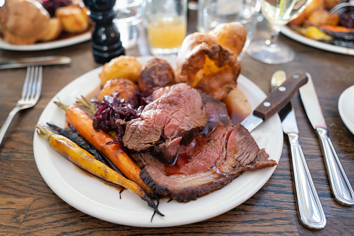 Roast beef on a white plate with roast potatoes and Yorkshire pudding with vegetables in a restaurant.