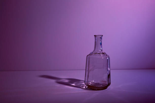 istock Glass empty open bottle with copy space. Graphic still life with light and shadow in lilac light. The concept of glass containers, recyclable materials or alcoholism. Large creative vase. Open flask 1356066466