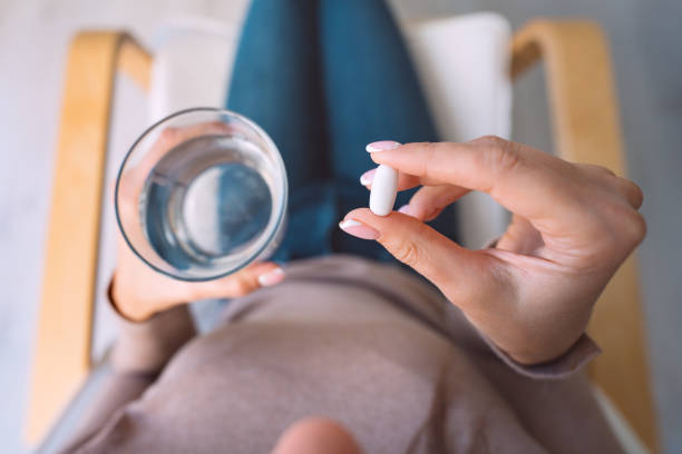 Woman holding glass of water and taking pill, medicine, antidepressant or antibiotic. Painkiller from headache or stomach pain Woman holding glass of water and taking pill, medicine, antidepressant or antibiotic. Painkiller from headache or stomach pain. High quality photo painkiller stock pictures, royalty-free photos & images