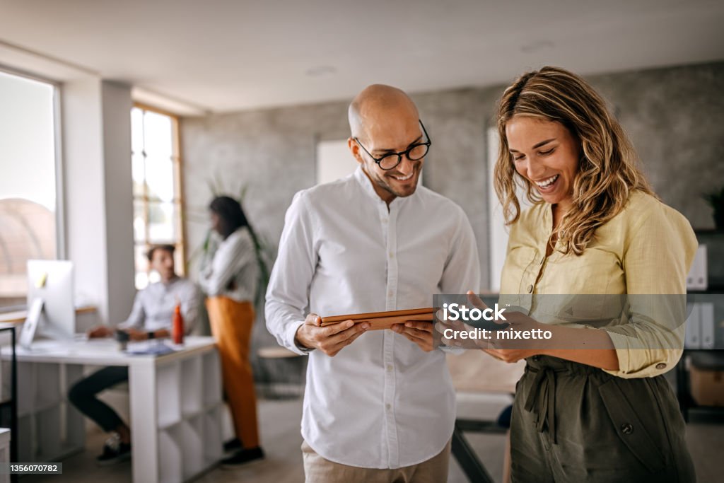 Businessman and businesswoman smiling looking at phone Cheerful and smiling young successful female businesswoman standing with colleague looking at smartphone in modern office and coworking space Office Stock Photo