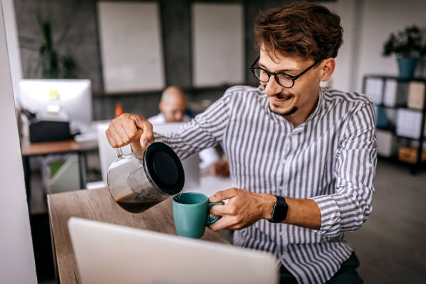 businessman pouring coffee at workplace - cup coffee pot coffee coffee cup imagens e fotografias de stock