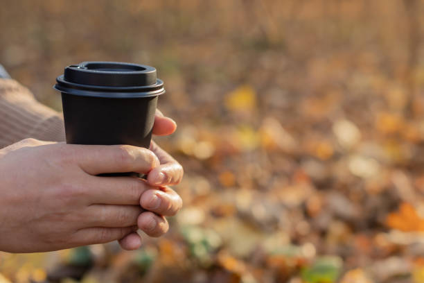 istock A man holds a disposable paper cup with a drink in the park in the fall. 1356078505