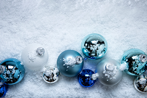 This is a photograph of blue and white and Silver Christmas ornaments shot in the snow on a white wooden background. There are no people in the photograph