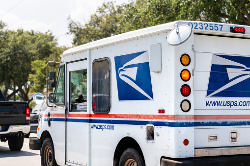 West Palm Beach, USA - July 8, 2021: Small USPS van truck delivering packages in Florida, on street road driving