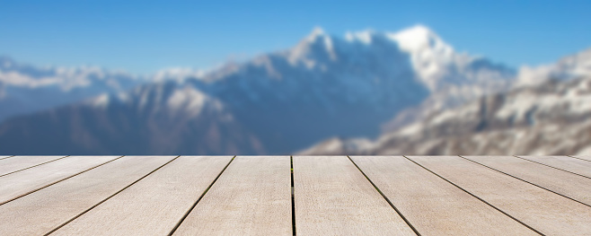 Empty wooden table in front of blurred background of snow mountain in winter season with blue sky among bright sunlight on a clear day. Can be used for display or montage for show your products.