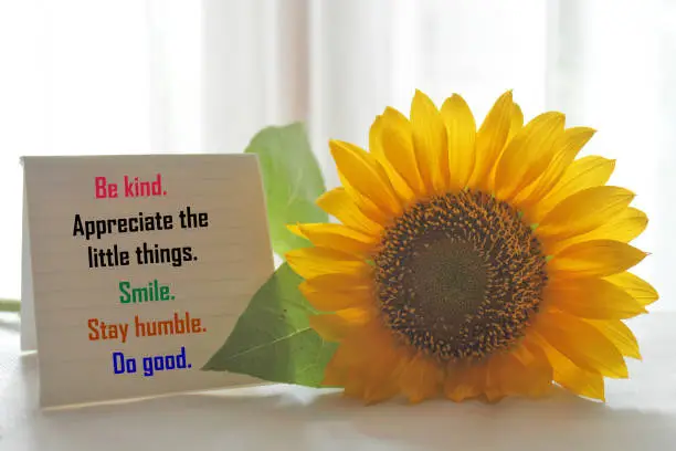 Photo of Sunflower and colorful positive messages on the table. Be kind. Appreciate the little things. Smile. Stay humble. Do good.