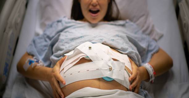 A woman in the delivery room, suffering from painful contractions. Child birth and labor. A woman holding her belly lying down on the hospital bed, screaming in pain from contractions. woman pushing tire stock pictures, royalty-free photos & images