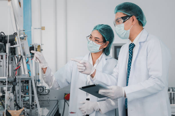 Both male and female Asian scientists are outfitted with protective gear. Examining the factory's machinery and materials used in the mask-making process. Covid19 is a piece of preventive equipment. tanto los científicos asiáticos masculinos como femeninos están equipados con equipo de protección. examinar la maquinaria y los materiales de la fábrica utilizados en el proceso de fabricación de máscaras. el covid 19 es un equipo preventivo.