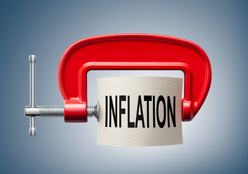 Paper note with Inflation written is compressed with a c-clamp isolated on blue background.