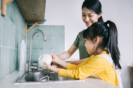 Mother and daughter wash the dishes together.