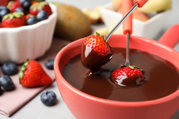 istock Dipping strawberries into fondue pot with chocolate on table, closeup 1356124907