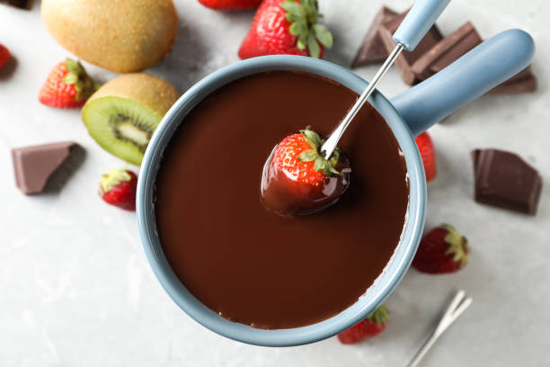 istock Dipping strawberry into fondue pot with chocolate on light table, top view 1356125092