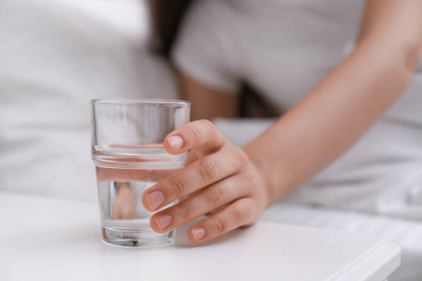 giovane donna che prende un bicchiere d'acqua dal comodino a casa, primo piano - comodino foto e immagini stock