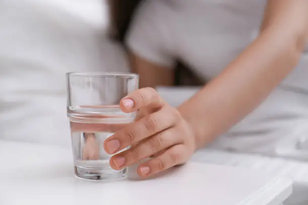 Young woman taking glass of water from nightstand at home, closeup