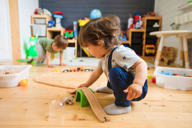 los niños pequeños juegan con un ferrocarril de madera en una guardería elegante. - niño pequeño fotografías e imágenes de stock