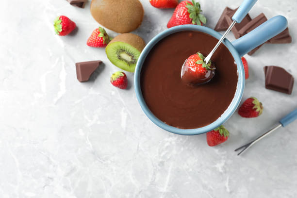 istock Dipping strawberry into fondue pot with chocolate on light grey marble table, top view. Space for text 1356126155