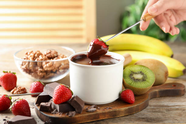 femme trempant des fraises dans un pot à fondue avec du chocolat à une table en bois, gros plan - fondue fork photos et images de collection