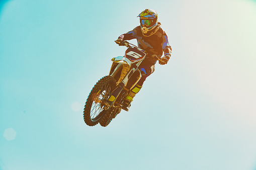 Extreme sports, motorcycle jumping. Motorcyclist makes an extreme jump against the sky. Extreme sports, motorcycle jumping. Motorcyclist makes an extreme jump against the sky. Special processing under the film with flare