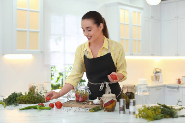istock Woman putting vegetables into pickling jar at table in kitchen 1356127521