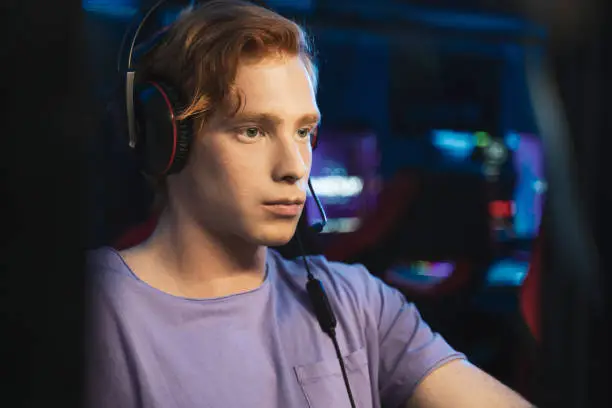 Photo of Player with headphones playing at popular online game while sitting with serious face