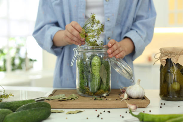 istock Woman putting dill into pickling jar at table in kitchen, closeup 1356132633