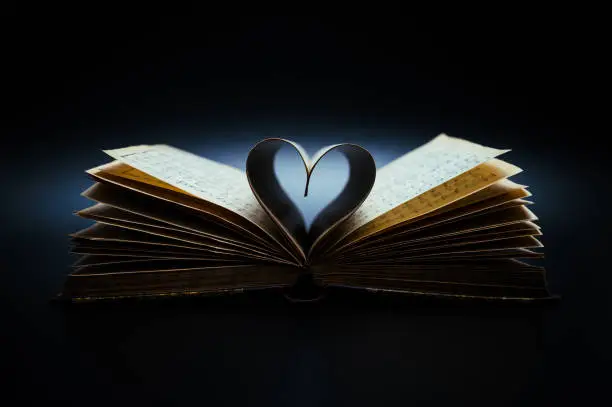 Opened, antiquarian book (19th century) with sheet music and pages curved into a heart shape on black background.