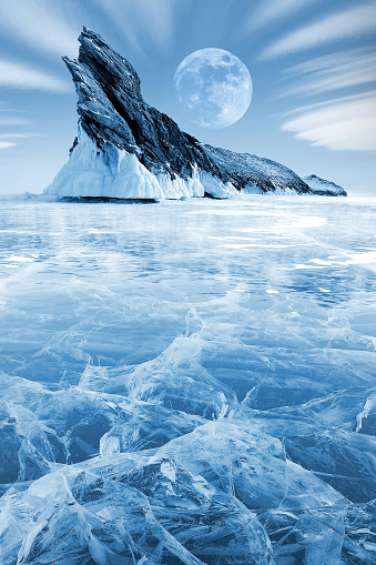 Winter Siberian landscape. Lake Bakal. Transparent patterned ice surface and mighty rock. Frosty blue image.