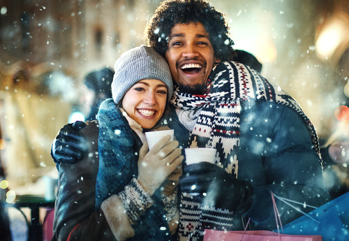 Closeup front view of a happy mid 20's mixed race couple walking through a street after shopping on a snowy Christmas eve.