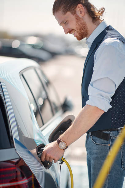 mężczyzna ładuje swój niezanieczyszczający pojazd elektryczny - nonpolluting zdjęcia i obrazy z banku zdjęć