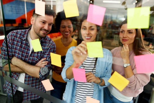 istock Group of web designers using sticky notes on a glass wall during a meeting 1356136823