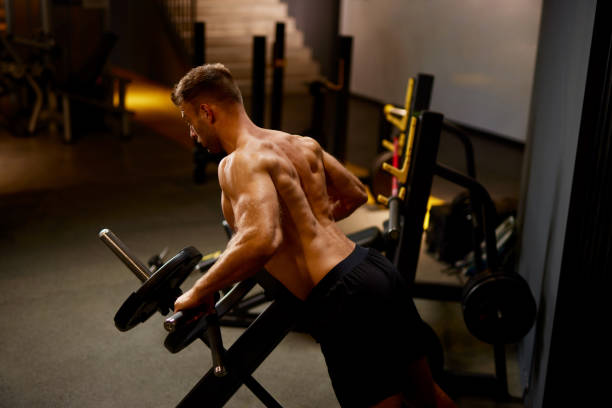 Muscular male bodybuilder exercising using fitness machine in a gym stock photo